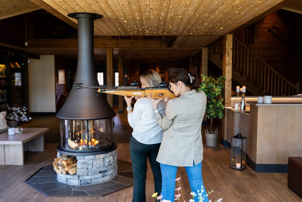 To kvinner øver på skiskyting innendørs foran sentralpeisen i lodgen på Skjelbreid Poirée Lodge