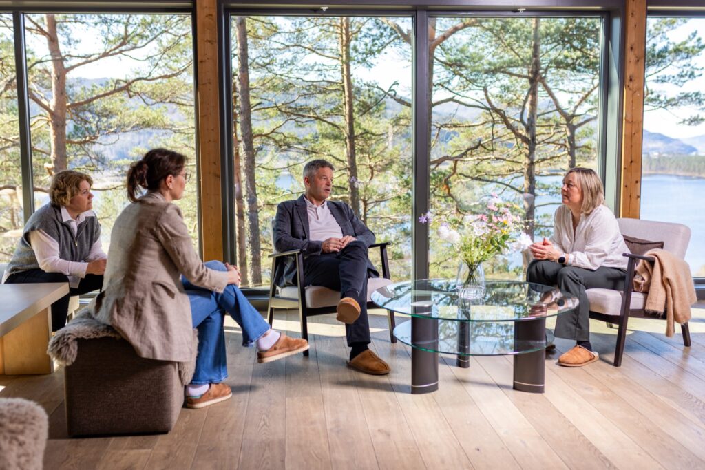 Fire personer i møte i lounge med store panoramavinduer mot fjord og skog på Skjelbreid Poirée Lodge